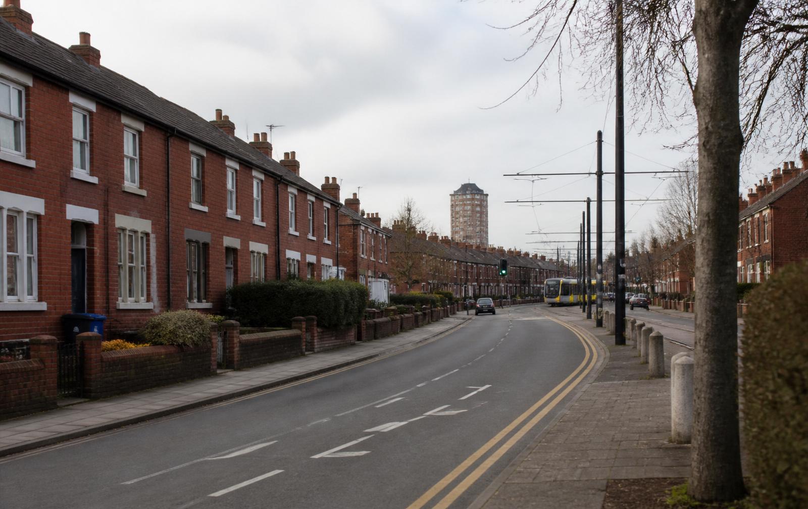 A quiet residential street in Trafford with red brick terraces and a passing tram